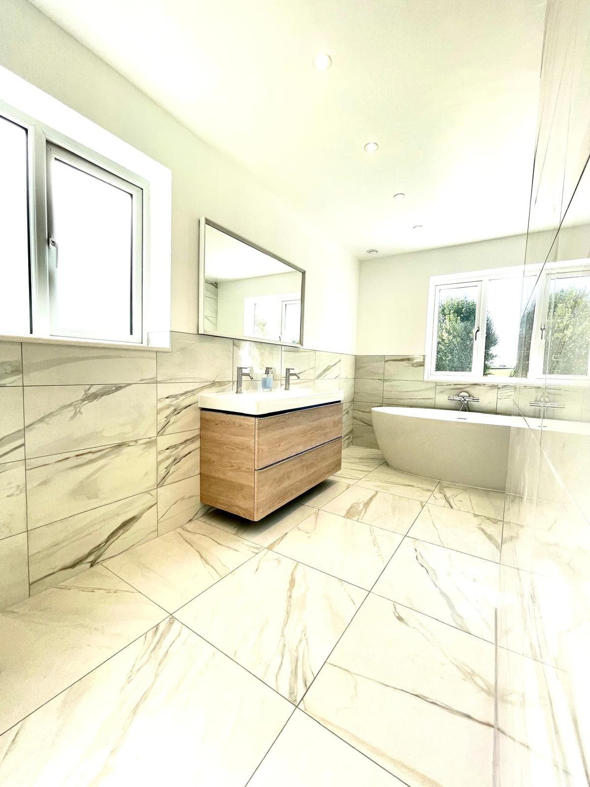 Bright ensuite bathroom with a freestanding oval bath, double-basin oak vanity unit and marble-effect tiling